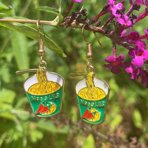 May include: A pair of gold-tone earrings featuring a green and white enamel noodle bowl with a red chili pepper and the word "NOODLES" on the front.