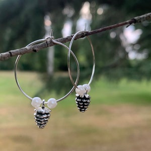 Puede incluir: Pendientes de aro de plata con un pequeño dije de piña y cuentas blancas que cuelgan de cada aro.