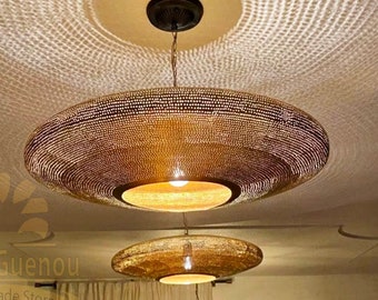May include: Two large, round, gold-toned metal pendant lights with a geometric pattern hang from a white ceiling. The lights cast a patterned shadow on the ceiling.