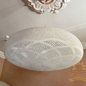May include: White metal pendant light fixture with a circular, domed shape and intricate cut-out design. The light fixture is hanging from a chain.
