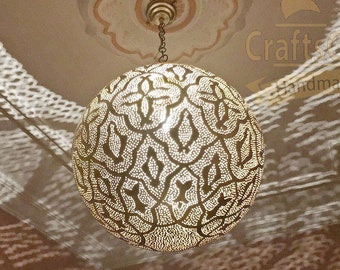 May include: A round, gold-coloured metal pendant light fixture with intricate cut-out designs. The light fixture is hanging from a ceiling with a white ceiling medallion.