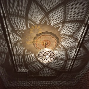 May include: A round, clear glass Moroccan pendant light with a brass frame and intricate geometric designs. The light casts a patterned shadow on the ceiling.