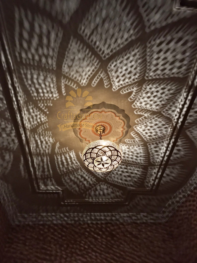 May include: A round, clear glass Moroccan pendant light with a brass frame and intricate geometric designs. The light casts a patterned shadow on the ceiling.