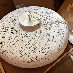 May include: White metal ceiling light fixture with a geometric pattern of holes. The light has a chain and a white metal canopy.