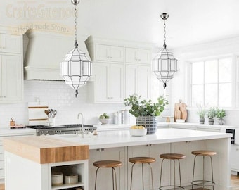 May include: A white kitchen island with a butcher block countertop and four wooden and metal bar stools. Two white pendant lights with geometric glass shades hang above the island.