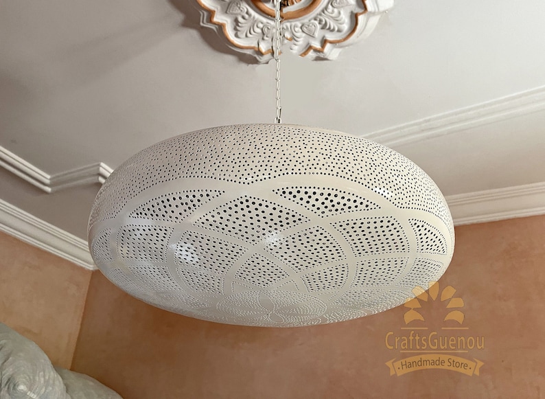 May include: White metal pendant light fixture with a circular, domed shape and intricate cut-out design. The light fixture is hanging from a chain.