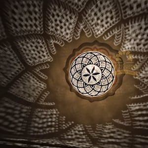 May include: A round, decorative ceiling light fixture with a geometric pattern. The light fixture is made of metal and has a gold finish. The light fixture is casting a shadow on the ceiling.