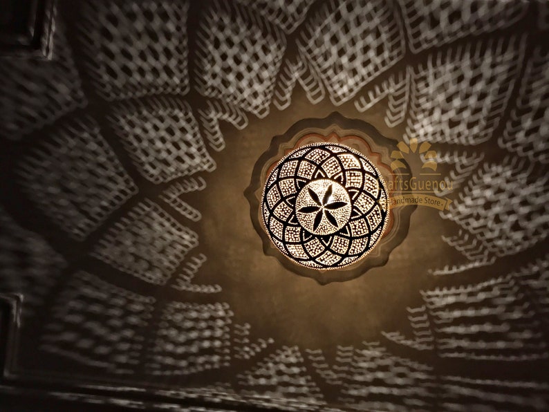 May include: A round, decorative ceiling light fixture with a geometric pattern. The light fixture is made of metal and has a gold finish. The light fixture is casting a shadow on the ceiling.