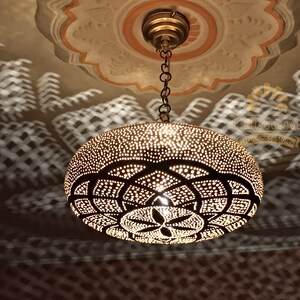 May include: A brass pendant light fixture with a geometric pattern and a chain hanging from the ceiling. The light fixture casts a shadow on the ceiling.