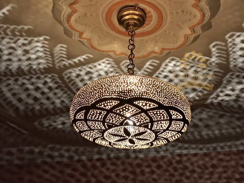 May include: A brass pendant light fixture with a geometric pattern and a chain hanging from the ceiling. The light fixture casts a shadow on the ceiling.