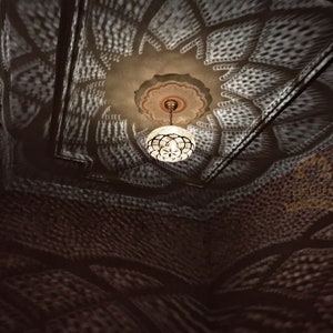 May include: A white ceiling with a decorative pattern of small circles and a chandelier hanging from the center. The chandelier is made of metal and has a round, white shade.