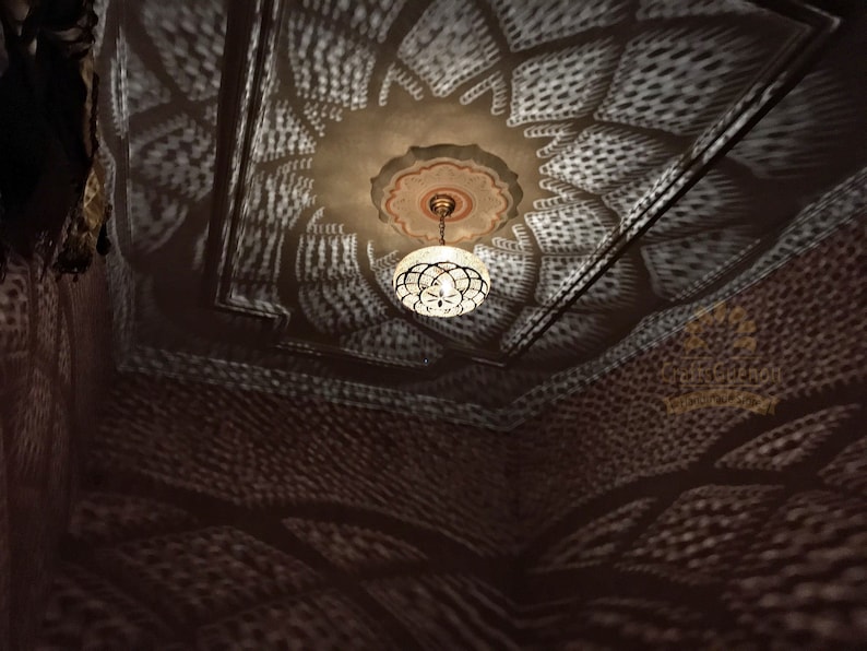 May include: A white ceiling with a decorative pattern of small circles and a chandelier hanging from the center. The chandelier is made of metal and has a round, white shade.