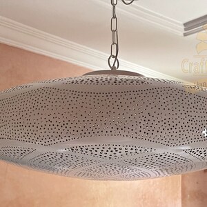 May include: White metal pendant light fixture with a round, perforated shade. The shade has a pattern of small, evenly spaced holes.