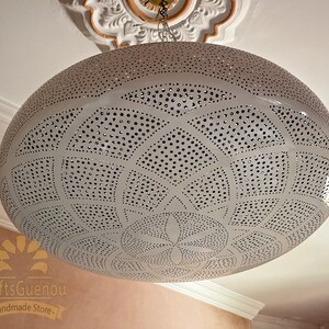 May include: White metal pendant light fixture with a circular, domed shape and intricate cut-out design. The light fixture has a delicate, geometric pattern with small holes throughout.