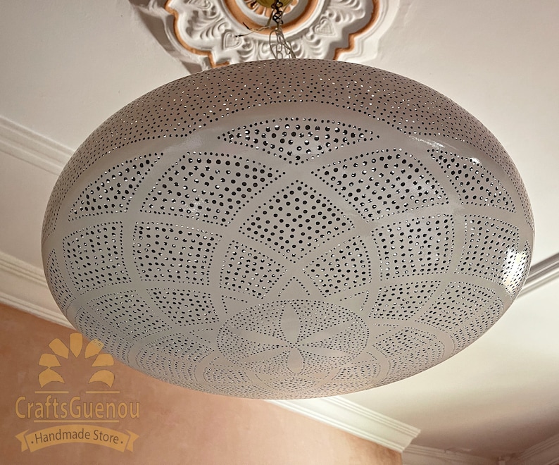 May include: White metal pendant light fixture with a circular, domed shape and intricate cut-out design. The light fixture has a delicate, geometric pattern with small holes throughout.
