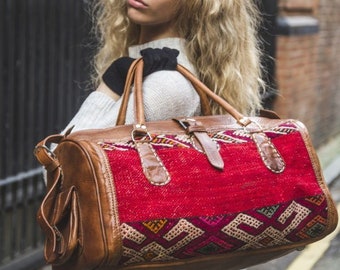 May include: A red and brown leather travel bag with a geometric pattern. The bag has a top handle and a shoulder strap.