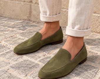 May include: A pair of olive green suede loafers featuring a low-cut silhouette, a rounded toe, and a dark brown sole. The shoes have a smooth, matte texture with visible stitching along the vamp and a simple, slip-on design for easy wear.