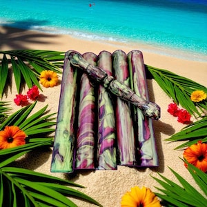 May include: A set of six colorful, patterned massage tools in shades of green, purple, and white. The tools are arranged on a sandy surface, with tropical flowers and foliage in the background. The tools are approximately 6 inches long.