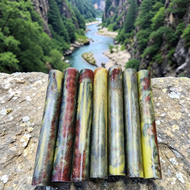 Pu&ograve; includere: Un set di sei pen blank cilindrici in resina caratterizzati da un motivo marmorizzato nelle tonalit&agrave; verde oliva, giallo e rosso scuro. Le superfici lisce e lucide mostrano variazioni di colore vorticose e pagliuzze metalliche.
