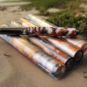 May include: A close-up of a silver and black pen with a white, black, and gold marbled design. The pen is lying on a pile of similar pens, all with the same marbled design.