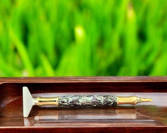 May include: A close-up of a pen with a white, triangular tip and a green and black marbled body. The pen is lying on a wooden surface.