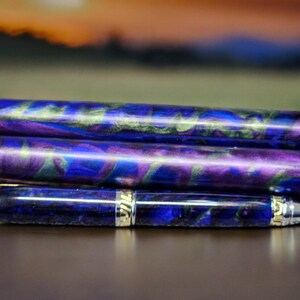 May include: Three blue, purple, and green marbled pen blanks stacked on top of a finished pen with gold accents.