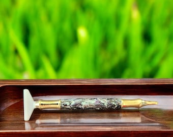 May include: A close-up of a pen with a white, triangular tip and a green and black marbled body. The pen is lying on a wooden surface.