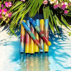 Puede incluir: Un conjunto de seis bolígrafos coloridos con un patrón de espiral. Los bolígrafos están hechos de resina y tienen un ribete dorado. Los bolígrafos están dispuestos en una fila, con las puntas apuntando hacia el espectador.