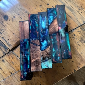 May include: A white ceramic mug with a black handle and the text "But First, Coffee" in a bold, black font. The mug is set against a blurred background, suggesting a cozy setting.