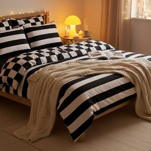 Puede incluir: Una cama con estructura de madera, con una funda nórdica y fundas de almohada a cuadros y rayas en blanco y negro. Una manta de punto color crema está sobre la cama. Una lámpara con forma de seta y velas están en una mesita de noche.