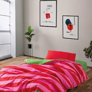 Puede incluir: Una cama con un edredón a rayas rojas y rosas y una almohada roja. La cama tiene una sábana bajera verde. Dos impresiones de arte abstracto enmarcadas cuelgan de la pared. Una planta en maceta está en la esquina.