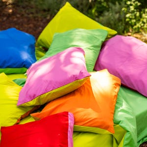 May include: A collection of colorful outdoor pillows in shades of blue, green, pink, orange, and red. The pillows are arranged on a green surface, creating a vibrant and inviting scene. The pillows appear to be made of a soft, durable fabric.
