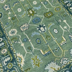 May include: A green rug with a geometric pattern in shades of blue, white, and green. The rug has a border with a more intricate design.