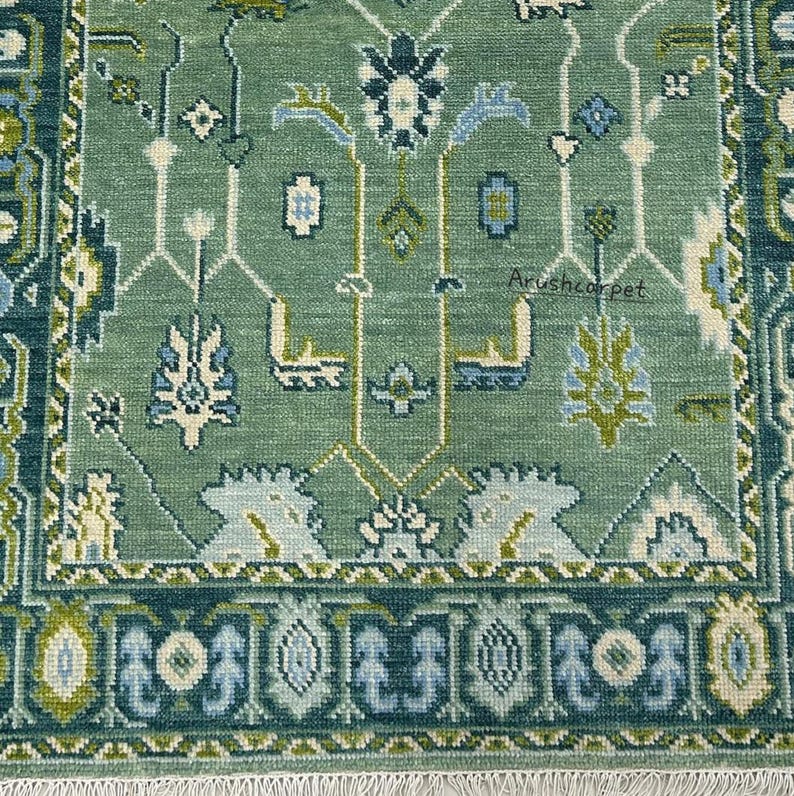 May include: A green rug with a traditional Persian design. The rug has a white fringe around the edges and features a repeating pattern of flowers and leaves.