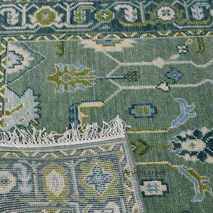 May include: A green rug with a traditional Persian design. The rug has a fringe border and features intricate floral patterns in shades of blue, green, and white.