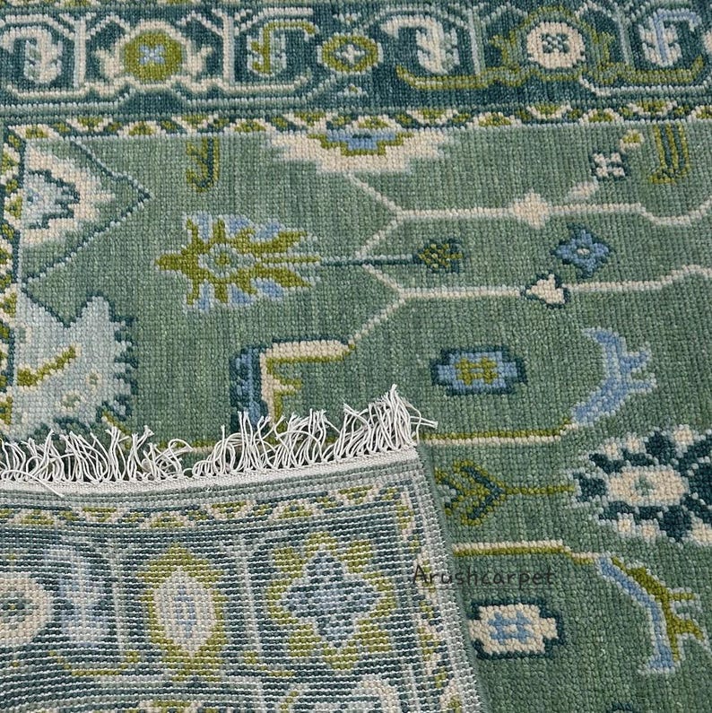 May include: A green rug with a traditional Persian design. The rug has a fringe border and features intricate floral patterns in shades of blue, green, and white.