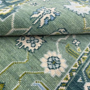 May include: Close-up of a green rug with a white and blue floral pattern. The rug has a soft, textured surface.