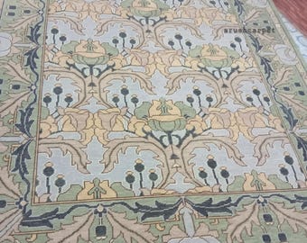 May include: A rectangular rug with a floral pattern in shades of green, beige, and blue. The design features stylized flowers and leaves, with a border of darker green and beige. The rug has a fringe along the bottom edge and the text "arushcarpet" is visible.