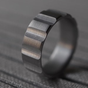 May include: A silver ring with a textured, ridged design. The ring is made of metal and has a polished finish.