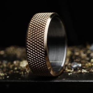 May include: A metallic ring with a textured, cross-hatched knurled exterior surface and a smooth, polished silver-toned interior band. The outer edge of the ring features a repeating diamond pattern, creating a tactile, industrial appearance.