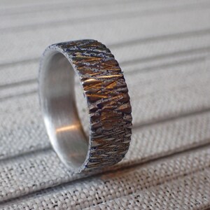 May include: A silver band with a textured, hammered finish. The band has a gold-toned accent.
