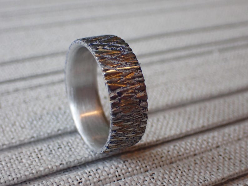May include: A silver band with a textured, hammered finish. The band has a gold-toned accent.