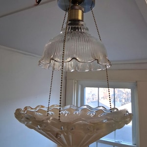 May include: Vintage glass chandelier with a clear, ribbed top shade and a frosted, scalloped bottom shade. The fixture is suspended by brass chains and a brass ceiling mount. The bottom shade has a decorative floral pattern.