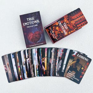 Puede incluir: Un juego de cartas de oráculo "TRUE EMOTIONAL" con un diseño en forma de corazón en la caja y el reverso de las cartas. Las cartas están abanicadas, revelando varias imágenes y la palabra "LOSING" en una carta. La caja dice "OIL PAINTING STYLE CARDS".