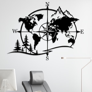 May include: A black metal wall art piece featuring a world map silhouette integrated with a compass rose, mountain peaks, and pine trees. The design includes the cardinal direction letters N, S, E, and W positioned at the compass points.
