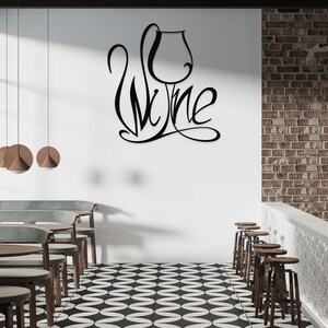 May include: Black metal wall art spelling "Wine" with a wine glass design. The art is mounted on a white wall in a bar or restaurant setting. The room features a black and white checkered floor, wooden tables, and bar stools.