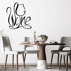 May include: Black metal wall art spelling "Wine" with a wine glass design. The art is mounted on a white wall above a table set for dining. The table has a wooden top and a marble base, surrounded by chairs.