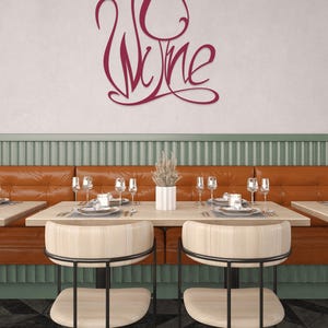 May include: A restaurant interior featuring a burgundy metal sign that reads "Wine" in a stylized script, with a wine glass design. The dining area includes tables, chairs, and a leather booth.