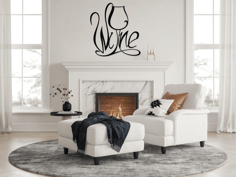 May include: Black metal wall art spelling "Wine" in a cursive font, with the "i" in the word forming the shape of a wine glass. The art is mounted on a white wall above a fireplace, with a white chair and ottoman in the foreground.