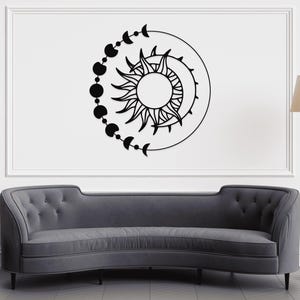 May include: Black wall art featuring a sun with radiating lines, a crescent moon, and a series of connected circles and crescent moons. The artwork is mounted on a white wall above a gray sofa.
